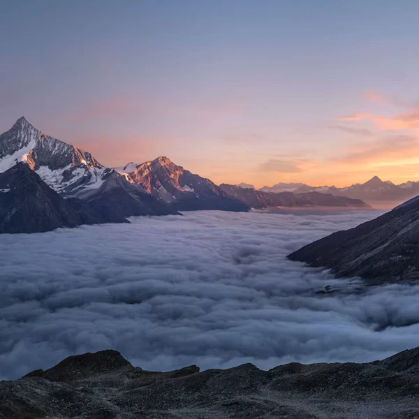Majestätische Berge über einem Meer aus Wolken im sanften Licht des Sonnenaufgangs