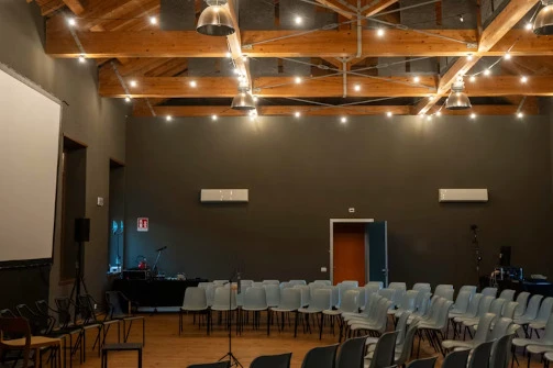 Konferenzsaal mit Reihenstühlen sichtbarer Holzdecke und zahlreichen warmen Edison-Glühbirnen als Beleuchtung